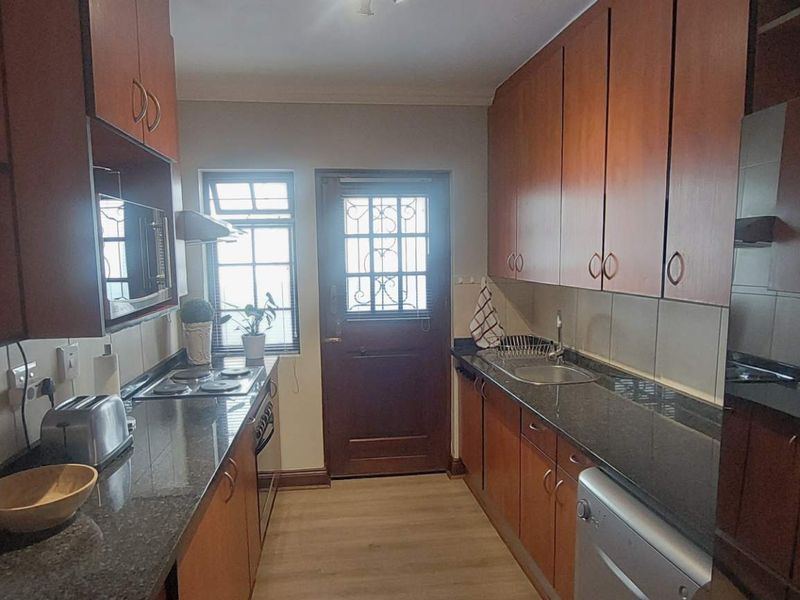 A functional galley-style kitchen featuring wood-finish cabinetry, granite countertops, and a secure exterior door leading outside.