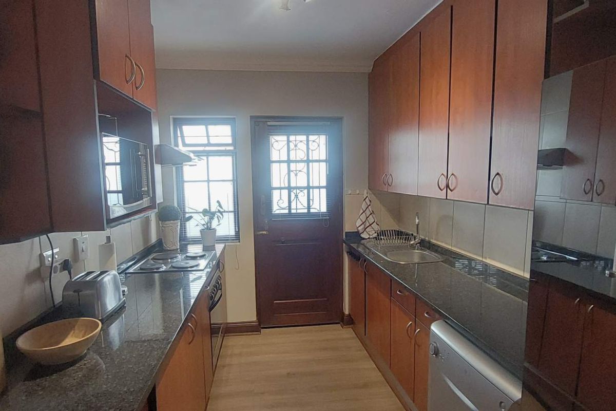 A functional galley-style kitchen featuring wood-finish cabinetry, granite countertops, and a secure exterior door leading outside.