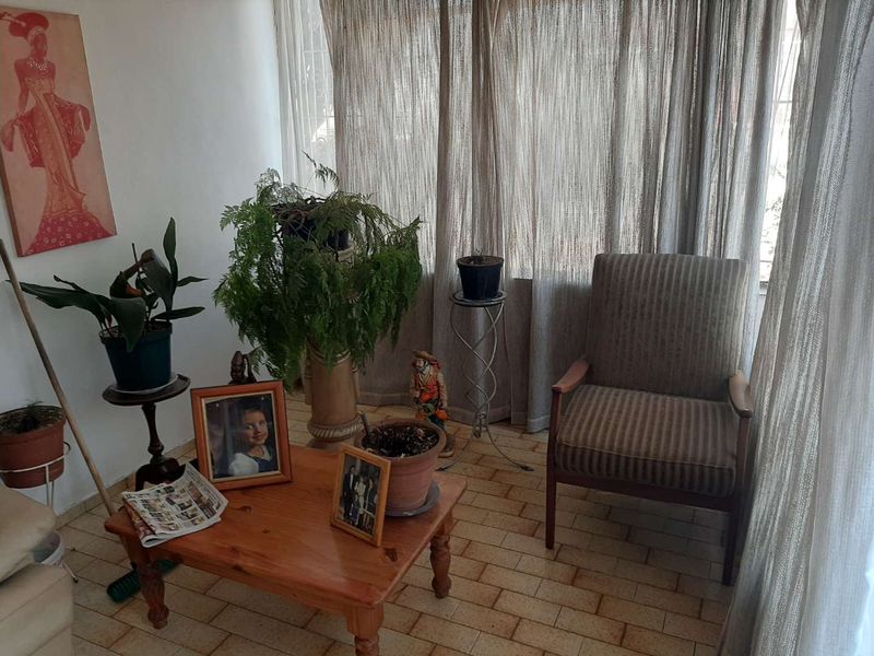 A sunlit living area featuring tiled flooring and large windows with floor-to-ceiling curtains, offering a bright and comfortable space.