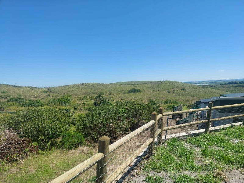 Expansive elevated view of the surrounding natural landscape and rolling hills, framed by a timber post and wire boundary fence.