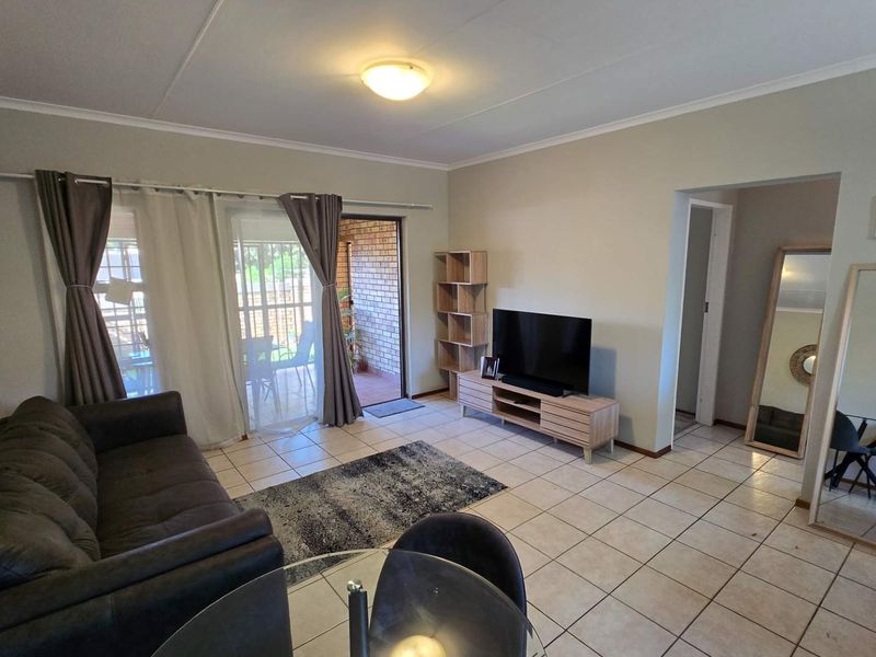 A bright living room featuring tiled flooring and a sliding glass door providing access to an outdoor patio area.
