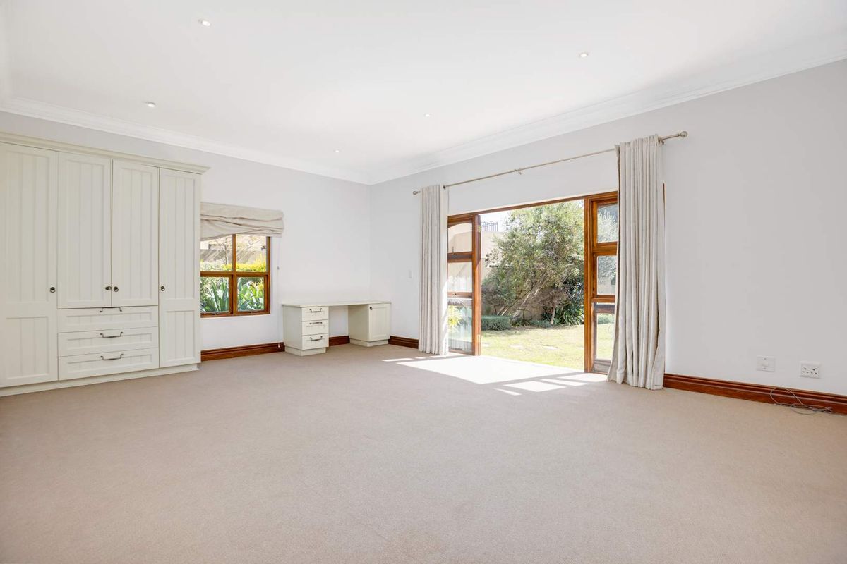 Spacious bedroom featuring built-in cabinetry, a fitted desk, neutral carpeting, and direct access to the garden through large wooden doors.