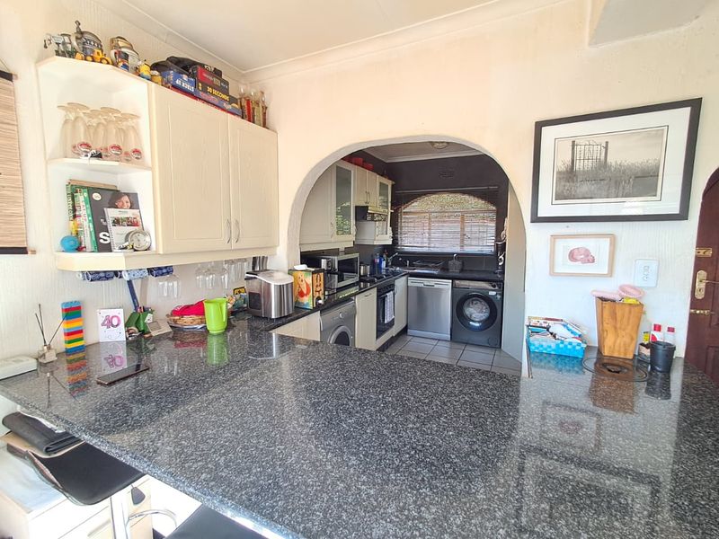 Open-plan kitchen featuring granite countertops, built-in cabinetry, and a functional scullery area with integrated appliances, connected by a classic architectural archway.