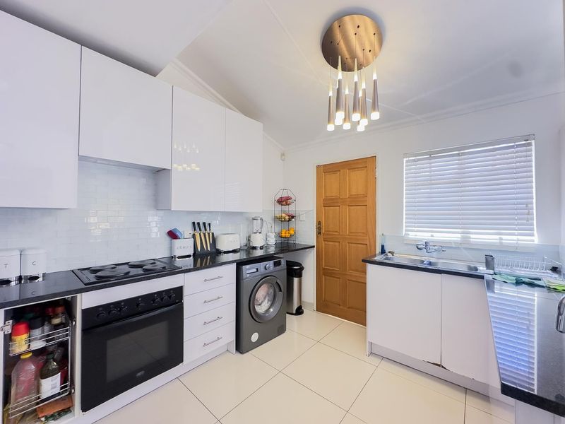 Modern kitchen featuring white cabinetry, black countertops, subway tile backsplash, built-in oven, electric hob, and a double sink with a window view.