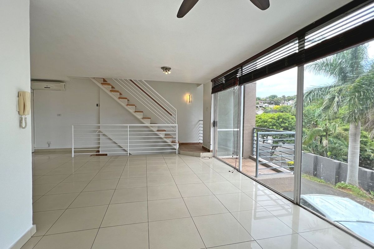 Spacious open-plan living area featuring large sliding glass doors leading to a balcony, tiled flooring, a staircase, and a wall-mounted air conditioning unit.