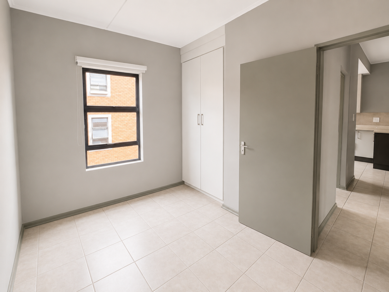 A clean, empty bedroom featuring neutral grey walls, tiled flooring, and a built-in wardrobe, offering a versatile space ready for personalization.