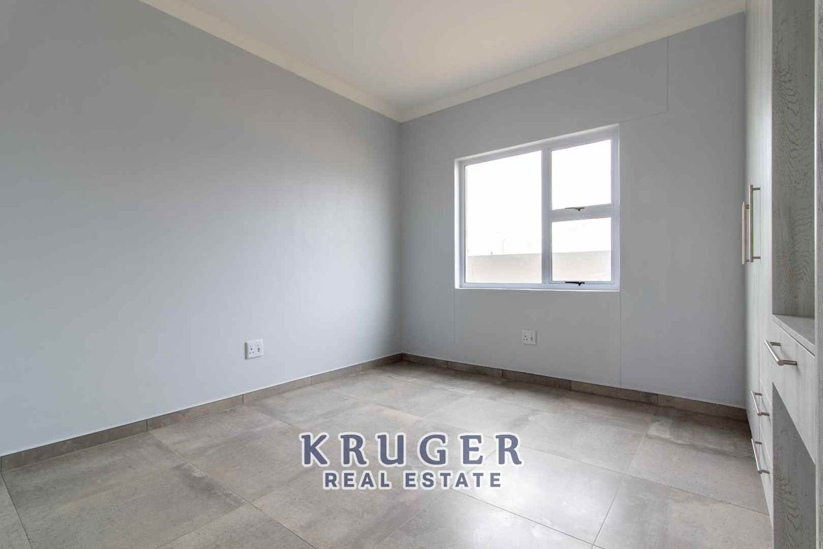 A bright, empty bedroom featuring neutral grey walls, large format floor tiles, and a built-in wardrobe.