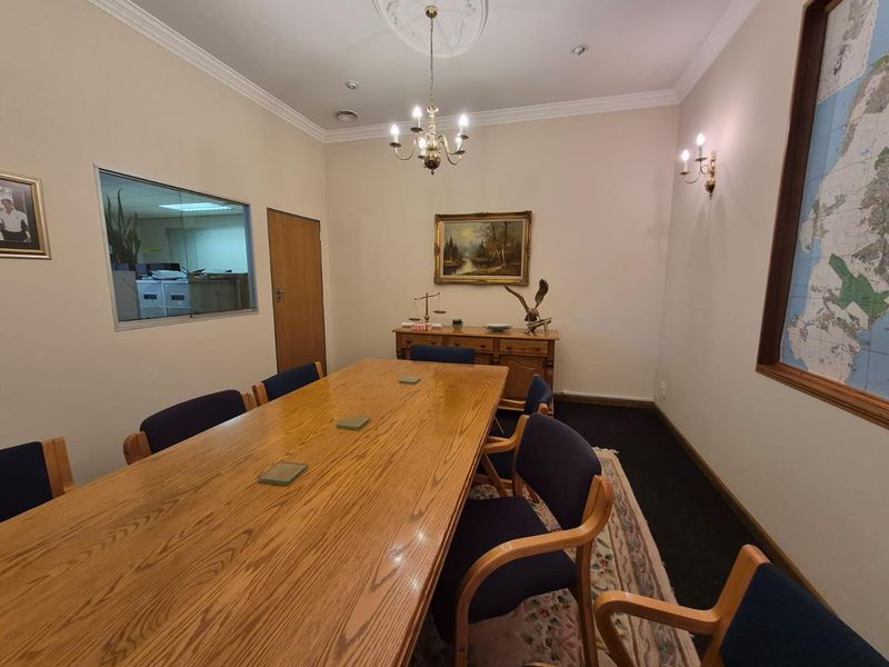 A professional office meeting room featuring a classic chandelier, decorative ceiling rose, wall sconces, and an internal viewing window looking into an adjacent workspace.