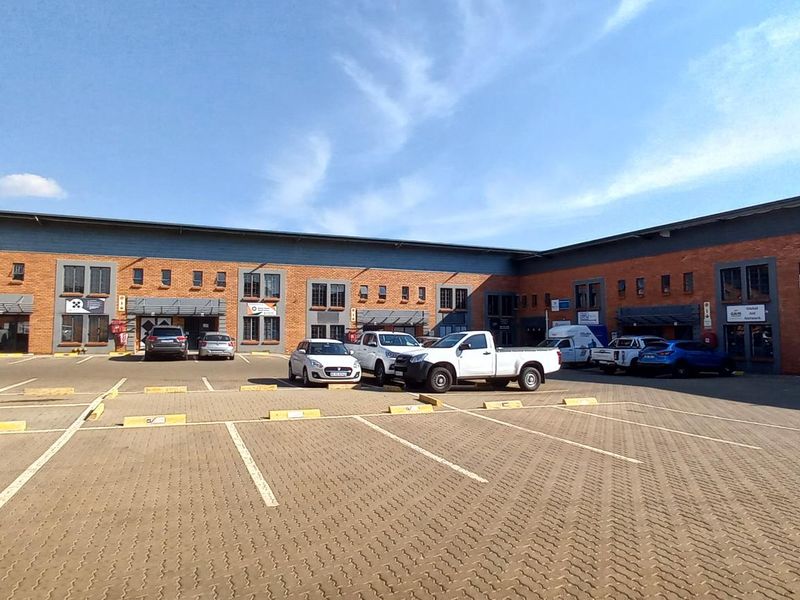 Exterior view of a modern industrial business park featuring brick facade, paved parking area, and multiple commercial unit entrances.