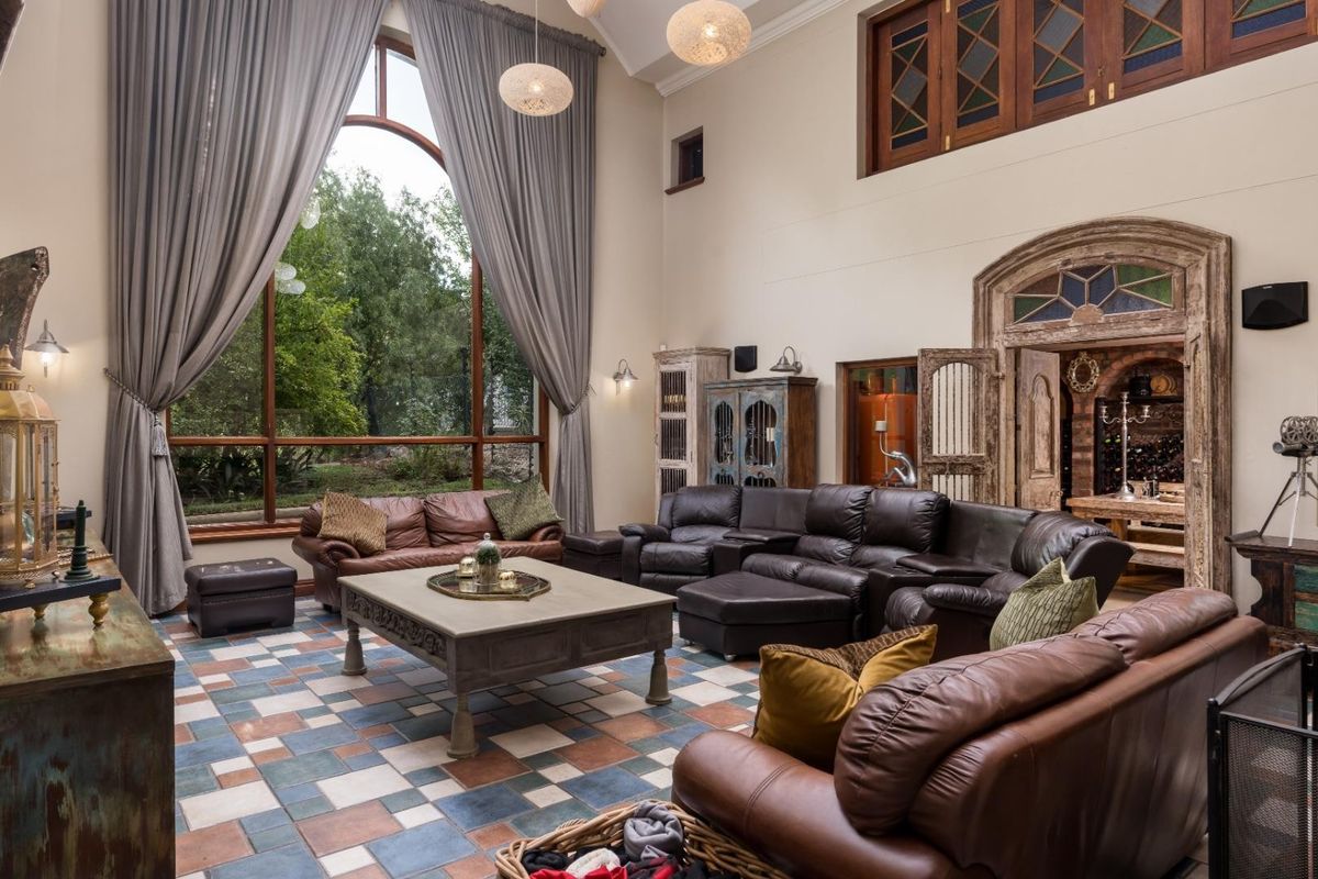 Spacious living room featuring double-volume ceilings, large arched windows, decorative stone-framed doorway, and unique multi-colored tiled flooring.