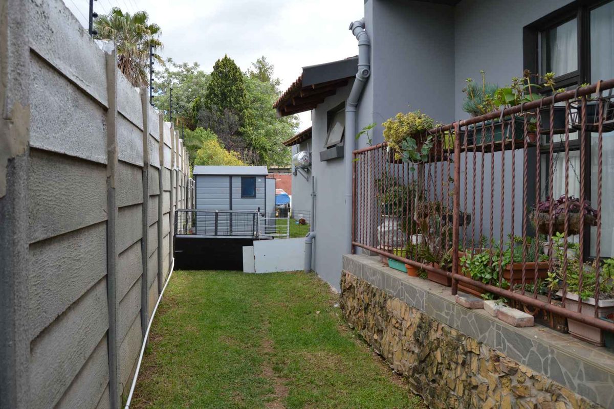 Side garden area featuring a precast concrete boundary wall with electric fencing, stone-clad foundation, and metal railing along the building exterior.