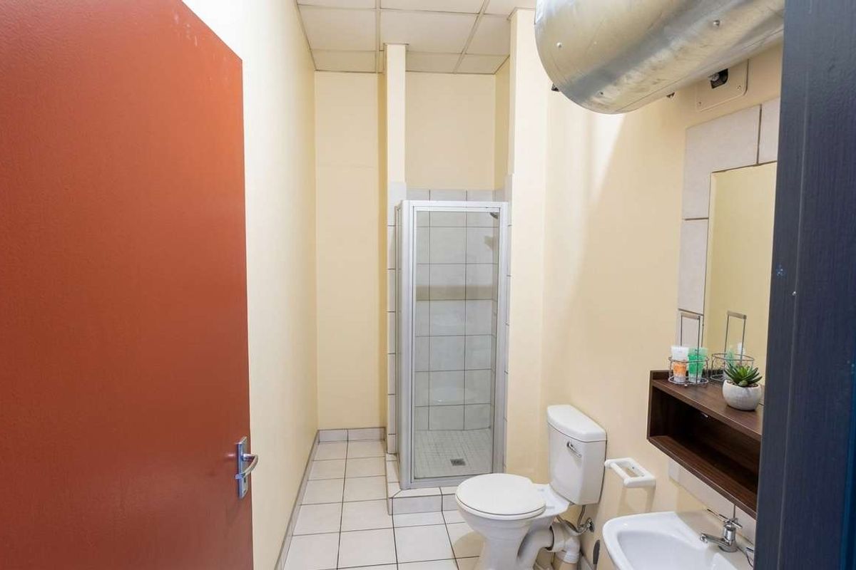 A functional bathroom featuring a shower cubicle, toilet, and wall-mounted basin with a mirror, finished with tiled flooring.