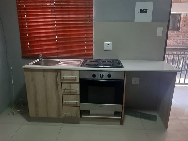 Compact kitchen area featuring built-in cabinetry, a stainless steel sink, and an integrated electric oven and hob with tiled flooring.