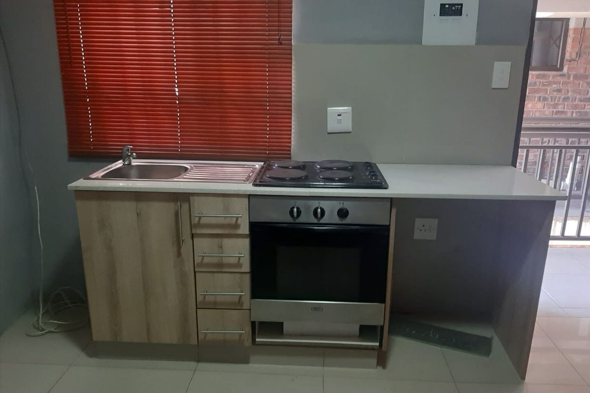 Compact kitchen area featuring built-in cabinetry, a stainless steel sink, and an integrated electric oven and hob with tiled flooring.
