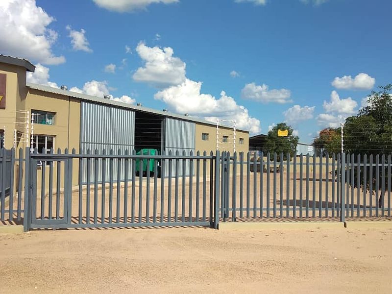 Front view of an industrial property featuring secure steel palisade fencing, electric security wires, and large sliding industrial access doors.