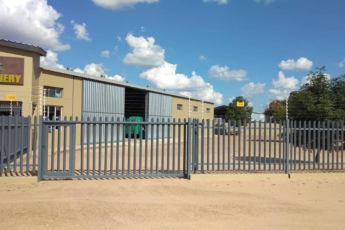 Front view of an industrial property featuring secure steel palisade fencing, electric security wires, and large sliding industrial access doors.