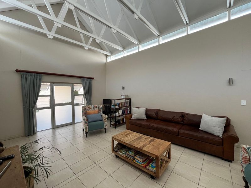 Spacious living room featuring high vaulted ceilings with exposed white trusses, clerestory windows for natural light, and neutral tiled flooring.