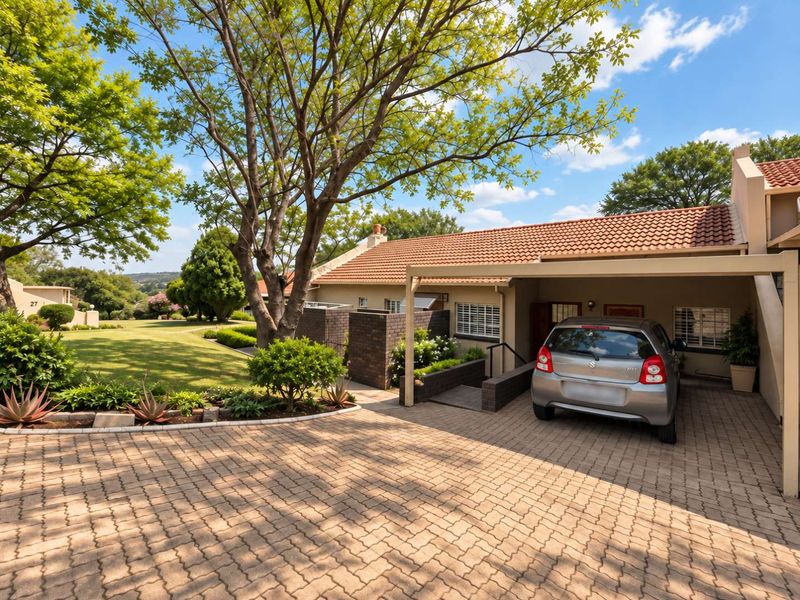 A well-maintained retirement village unit featuring a paved driveway, covered carport, and established garden surroundings with a classic tiled roof facade.