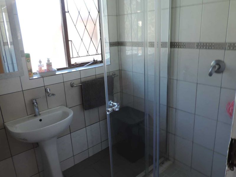 A functional bathroom featuring a pedestal basin, tiled walls, and a glass-enclosed shower with security bars on the window.