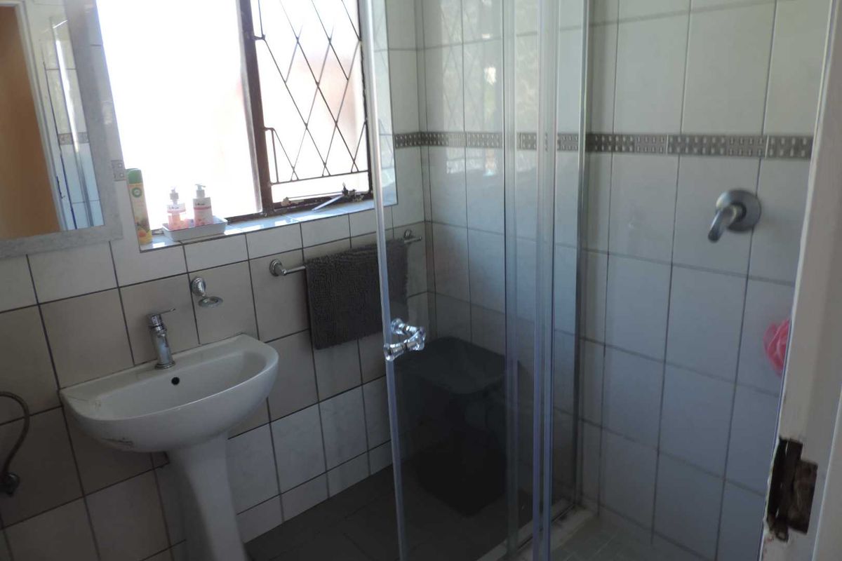 A functional bathroom featuring a pedestal basin, tiled walls, and a glass-enclosed shower with security bars on the window.