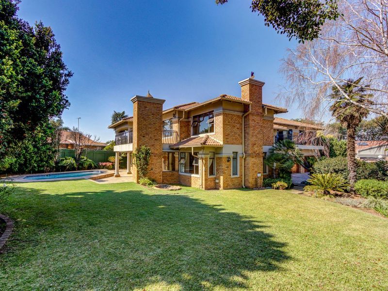 A spacious rear view of the brick house featuring a well-maintained garden, swimming pool, and upper-level balconies.
