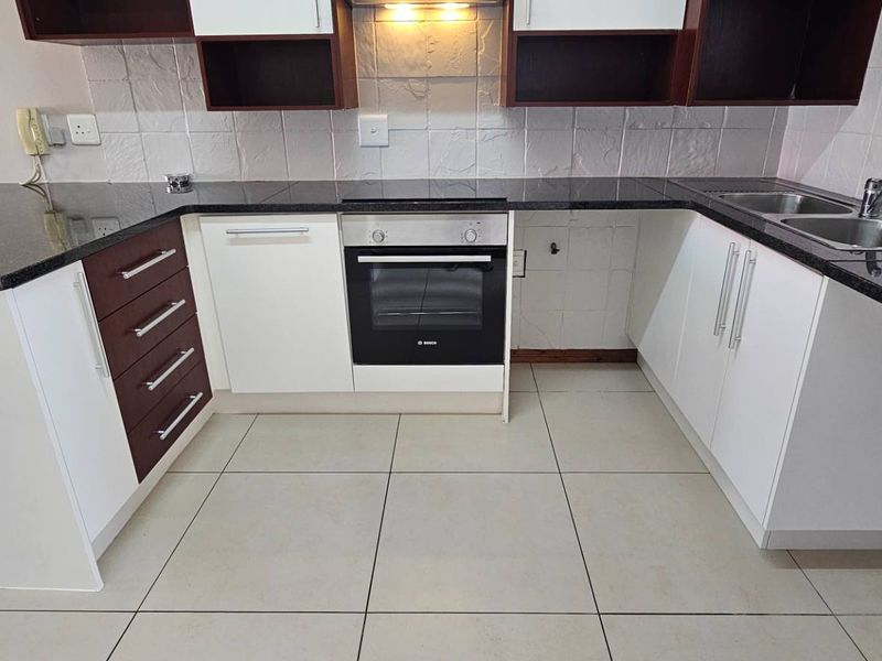 A functional kitchen featuring dark granite countertops, built-in oven, extractor fan, and ample cabinetry with a double basin sink and tiled flooring.