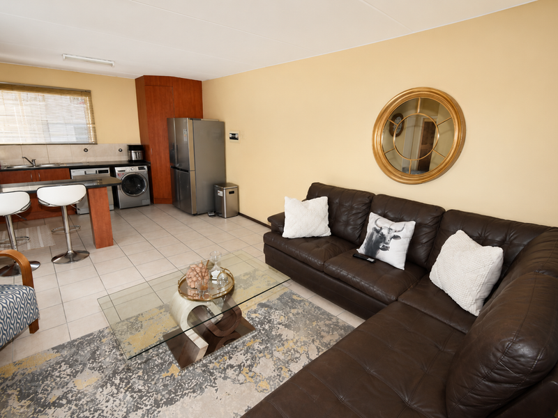 Open-plan living area featuring a functional kitchen with breakfast bar, tiled flooring, and integrated cabinetry, seamlessly connecting to the lounge space.