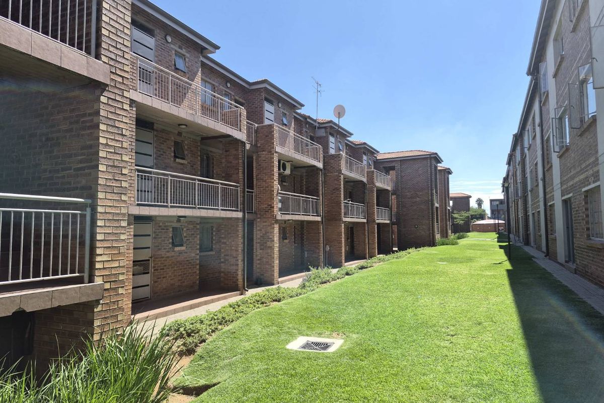 Exterior view of a multi-story apartment complex featuring face brick facades, private balconies with metal railings, and a well-maintained communal garden area.