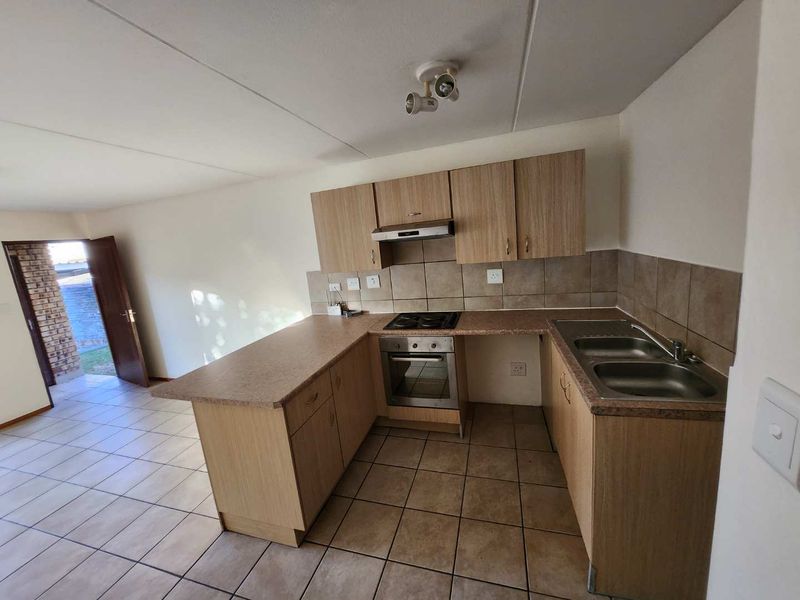 Functional kitchen featuring laminate cabinetry, built-in oven, hob, extractor fan, and double bowl stainless steel sink with tiled backsplash and flooring.