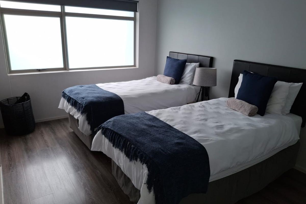 A well-maintained bedroom featuring laminate flooring, a large window with a roller blind, and space for two single beds.