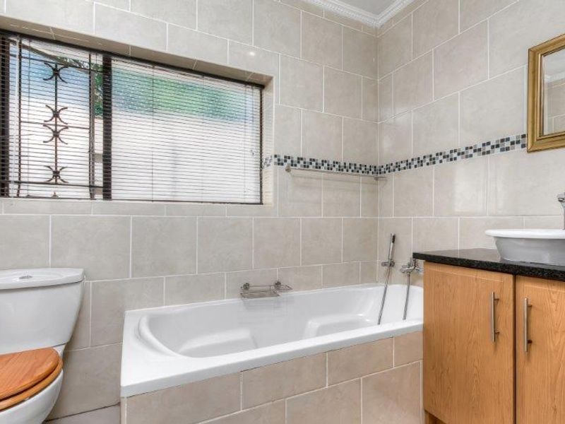 A well-maintained bathroom featuring a built-in bathtub, a modern vessel sink on a wooden vanity cabinet, and neutral ceramic wall tiling.