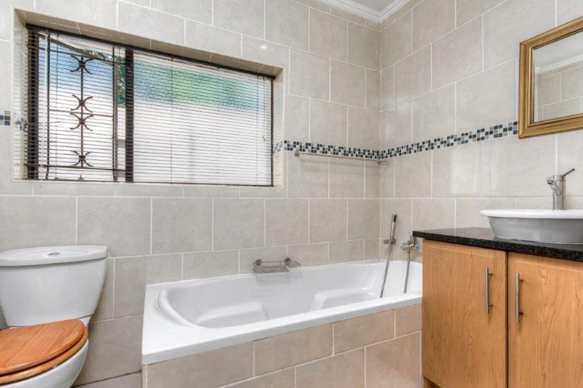 A well-maintained bathroom featuring a built-in bathtub, a modern vessel sink on a wooden vanity cabinet, and neutral ceramic wall tiling.