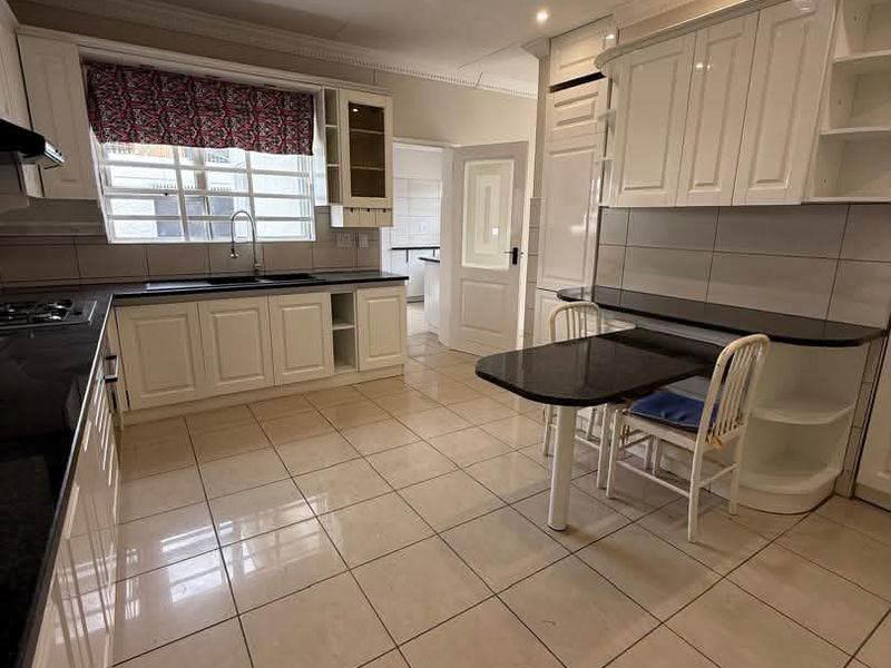 A well-maintained kitchen featuring white cabinetry, dark granite countertops, tiled flooring, and a built-in breakfast nook with recessed lighting.