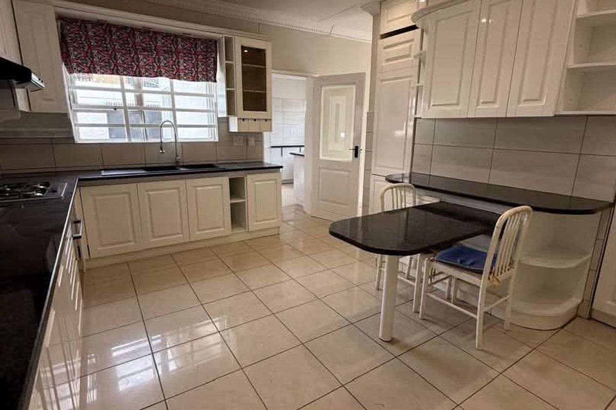 A well-maintained kitchen featuring white cabinetry, dark granite countertops, tiled flooring, and a built-in breakfast nook with recessed lighting.