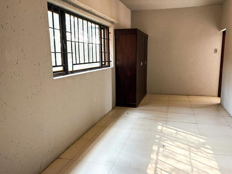 A bedroom featuring tiled flooring and security bars on the window. The room requires cosmetic updates to the wall finishes.