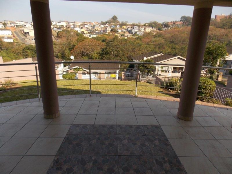 A covered patio featuring tiled flooring, structural columns, and a stainless steel balustrade, offering an elevated view of the surrounding residential area.