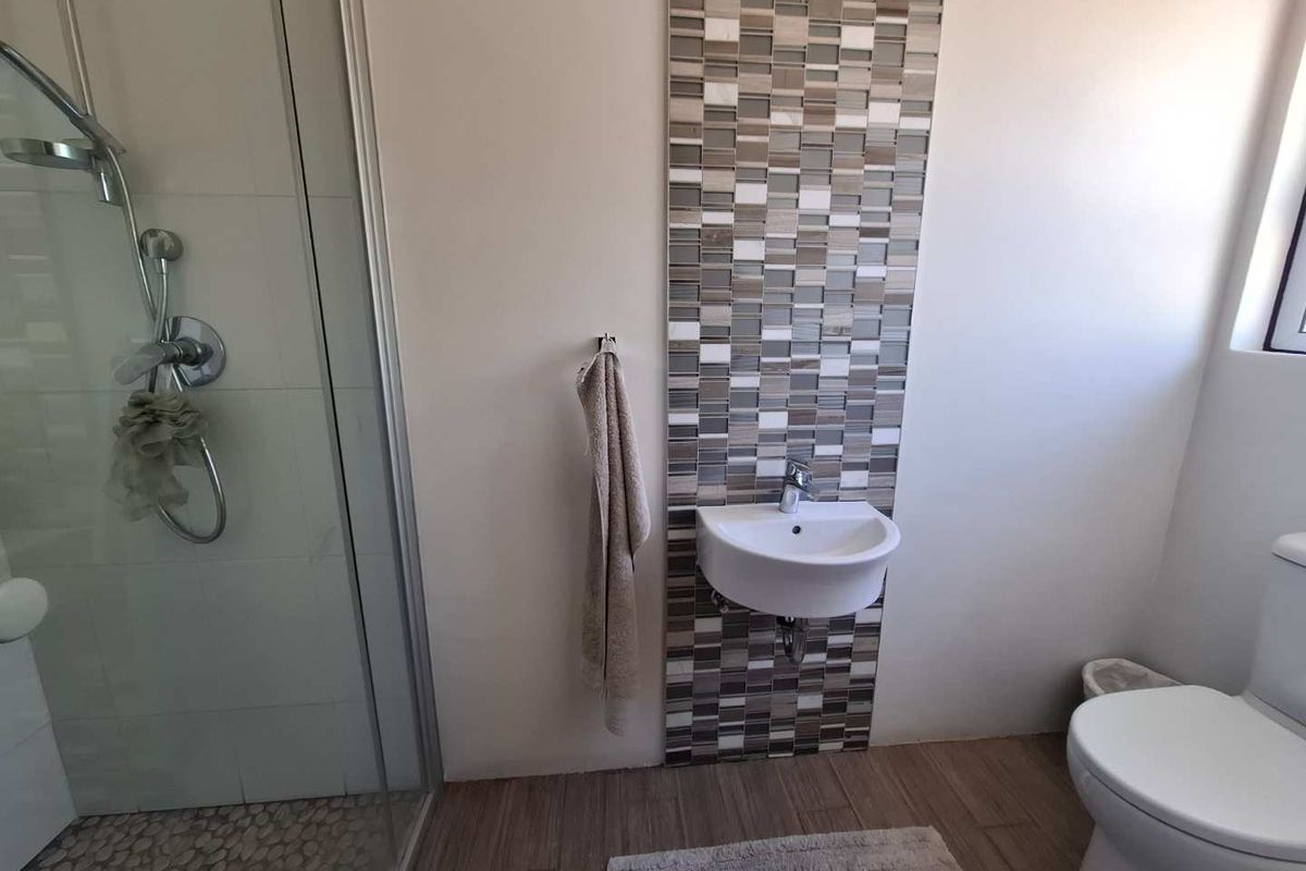 A modern bathroom featuring a glass-enclosed shower, a wall-mounted basin with decorative mosaic tile backsplash, and a standard toilet.