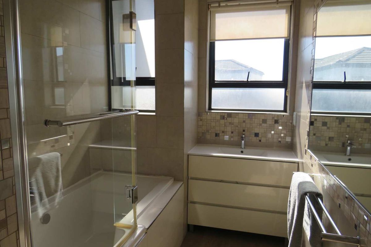 A modern bathroom featuring a built-in bathtub with a glass shower screen, a vanity unit with a basin, and tiled wall finishes.