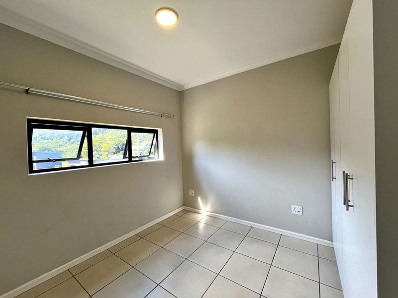 A clean, empty bedroom featuring neutral tiled flooring, built-in cupboards, and an aluminium-framed window with natural light.