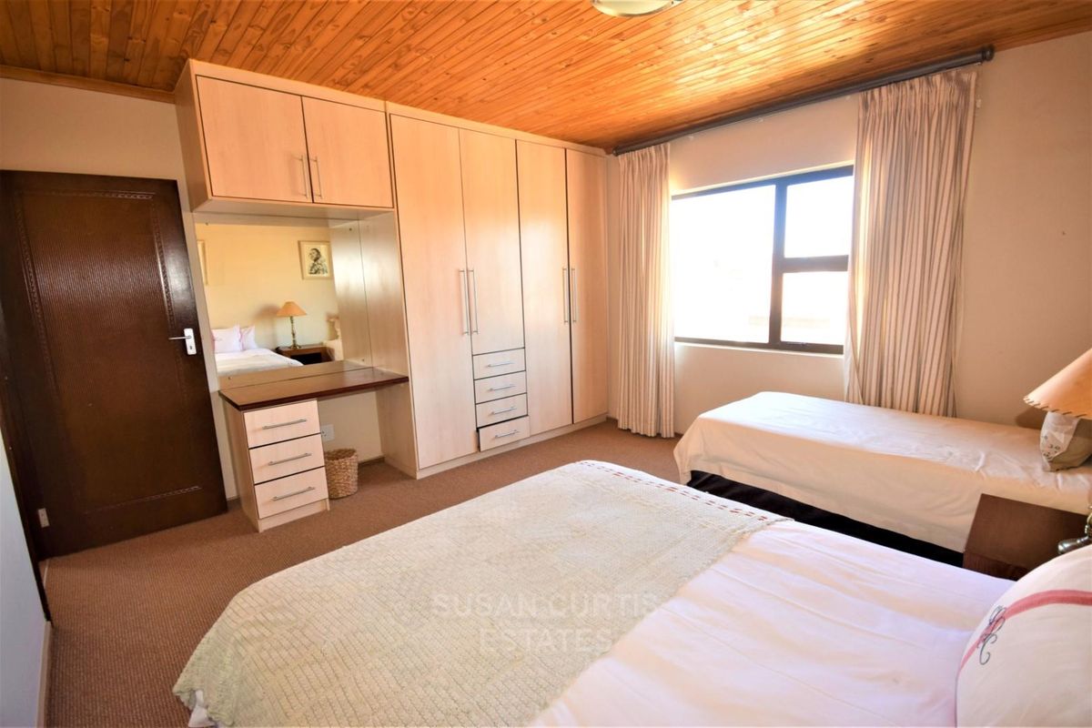 A bedroom featuring built-in cupboards with an integrated vanity, timber ceiling, and carpeted flooring.