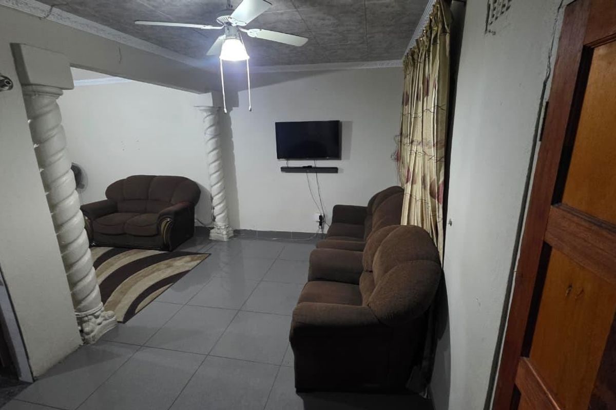 Living room featuring tiled flooring, decorative columns, and a ceiling fan, with visible wear to wall and ceiling finishes.