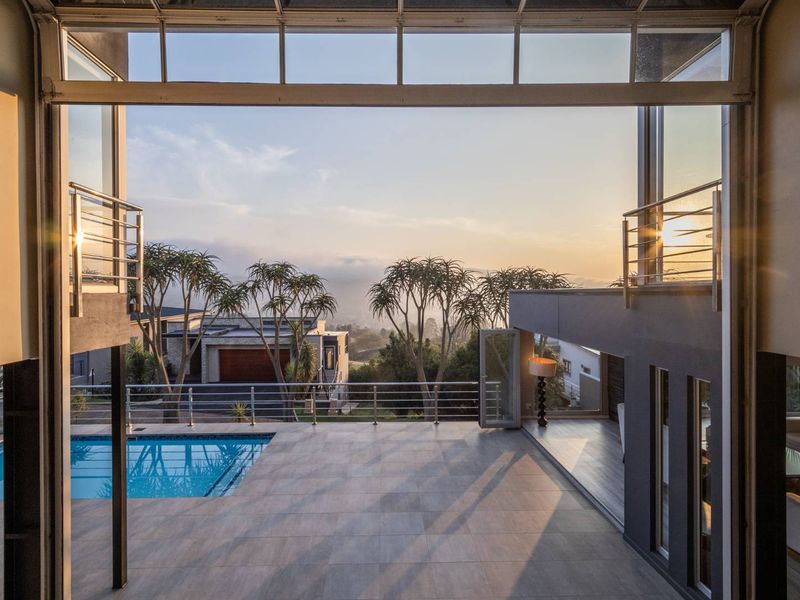 A modern covered patio featuring tiled flooring and stainless steel balustrades, overlooking a swimming pool with expansive views of the surrounding landscape.
