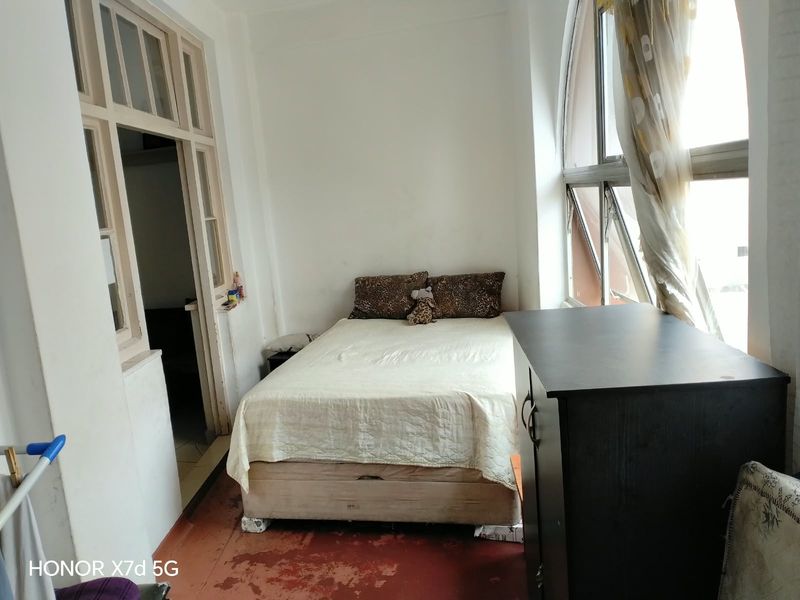 A bedroom featuring an arched window and traditional timber door frames, requiring cosmetic updates to the flooring and paintwork.