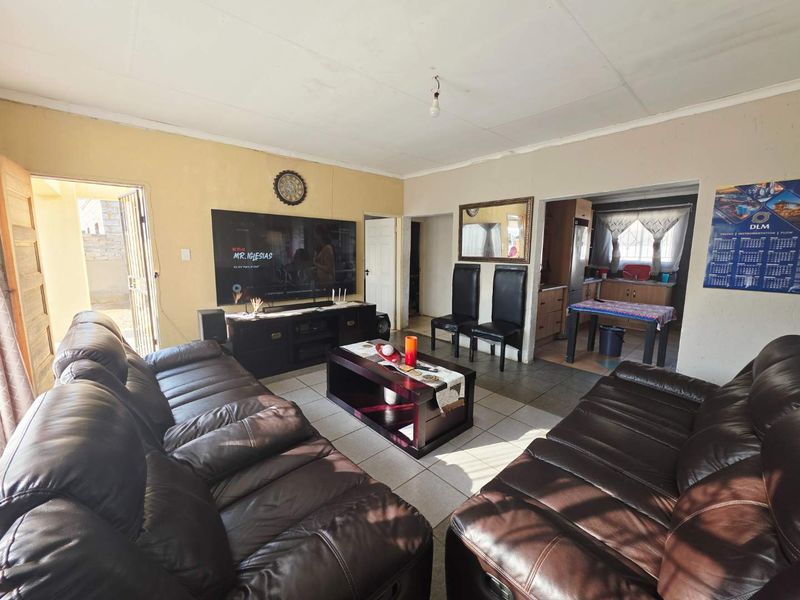 Open plan living area featuring tiled floors and an adjoining kitchen space with built-in cabinetry, providing a functional layout for daily living.