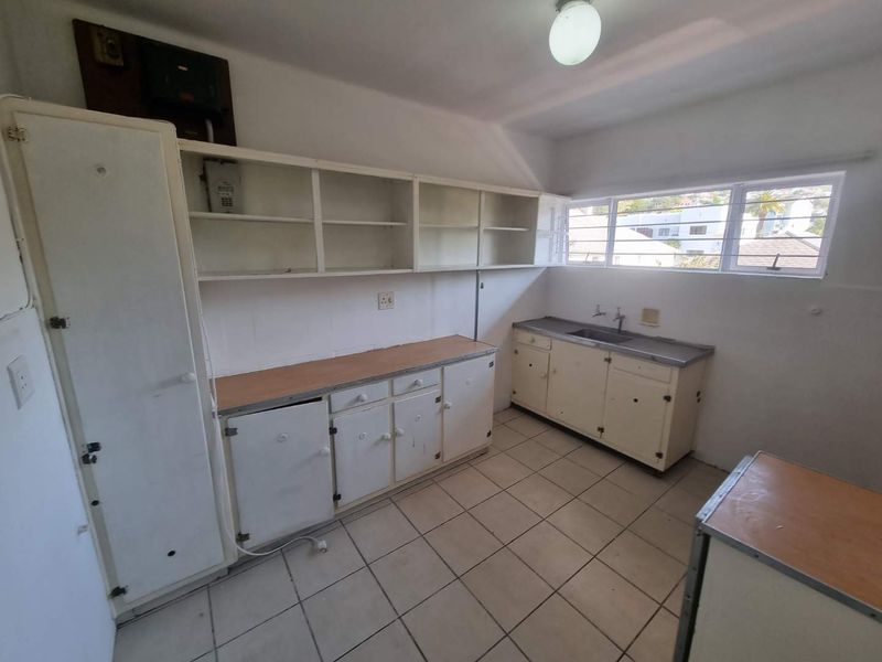 A functional, empty kitchen featuring built-in cabinetry, laminate countertops, a stainless steel sink, and ceramic floor tiles, ready for modernization and renovation.
