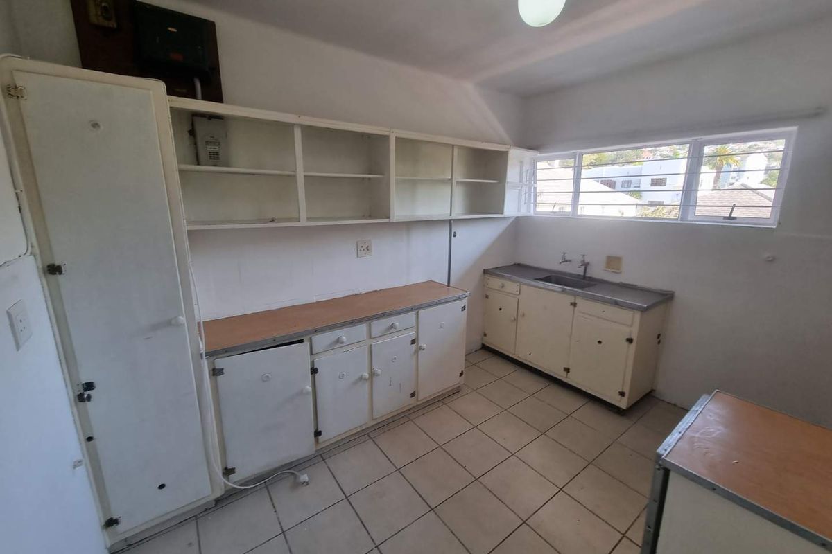 A functional, empty kitchen featuring built-in cabinetry, laminate countertops, a stainless steel sink, and ceramic floor tiles, ready for modernization and renovation.
