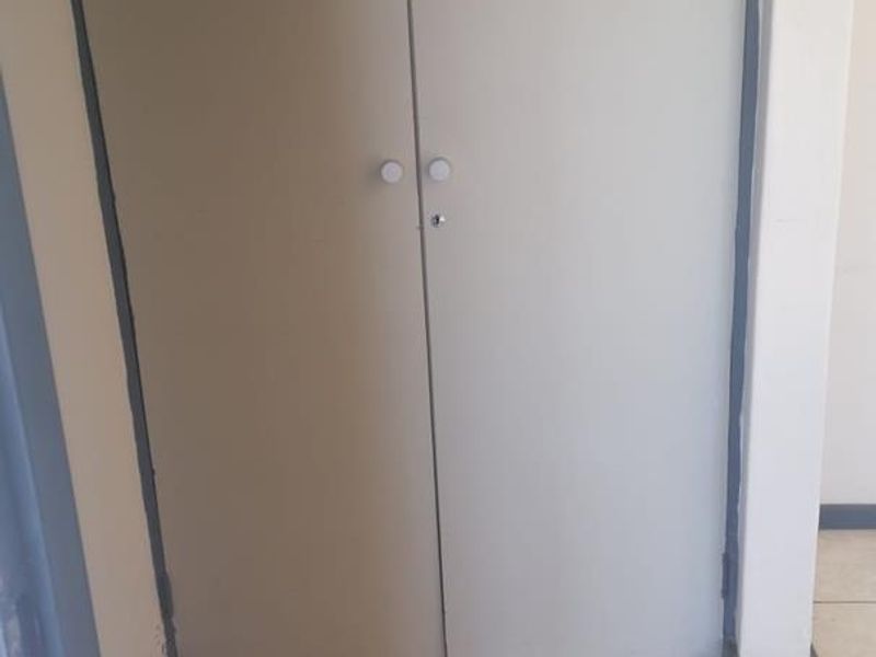 A hallway area featuring built-in storage cupboards with tiled flooring, showing signs of wear on the door frames.