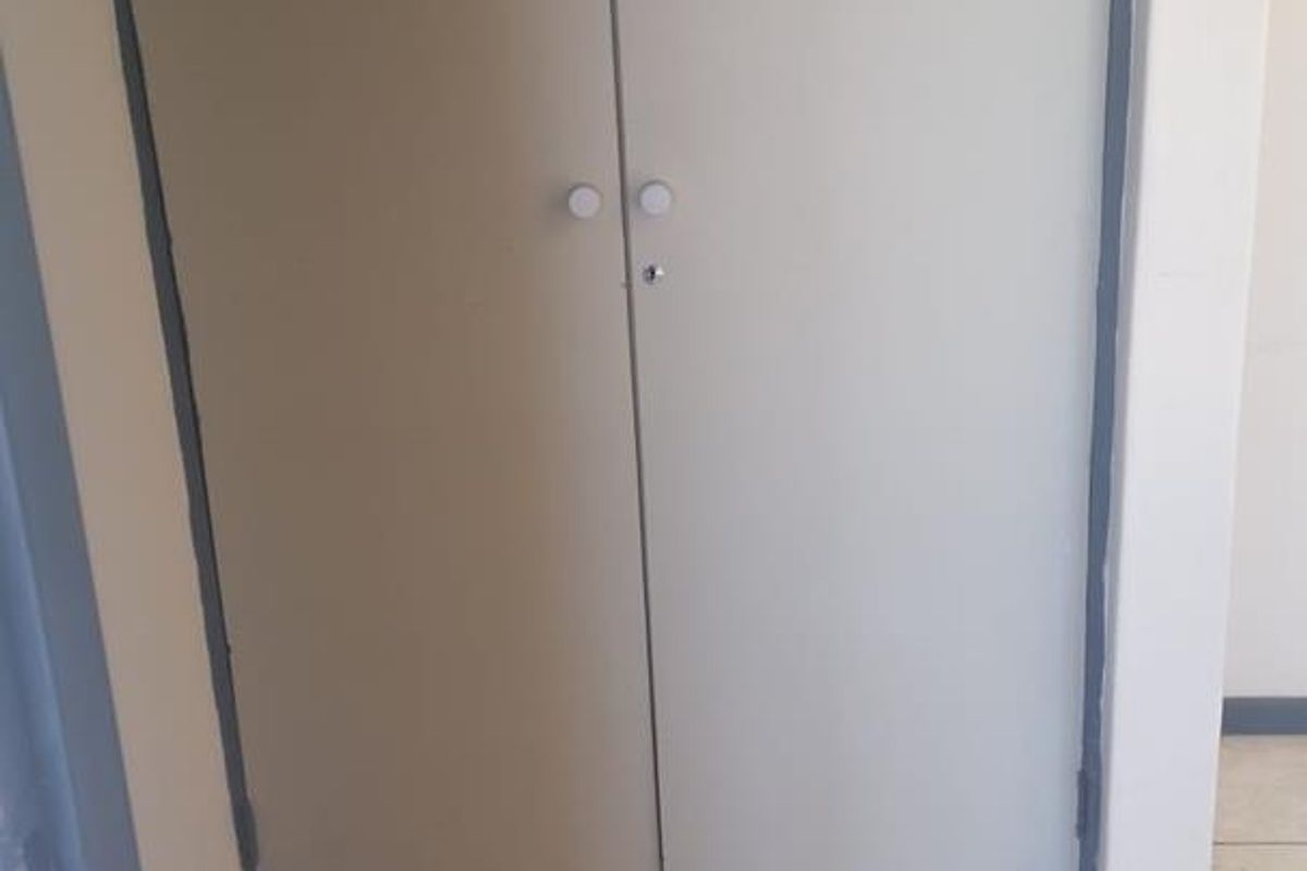 A hallway area featuring built-in storage cupboards with tiled flooring, showing signs of wear on the door frames.