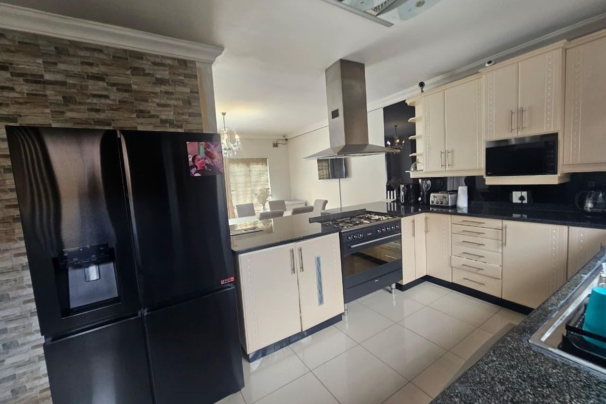 A well-appointed kitchen featuring cream cabinetry, granite countertops, a gas hob with stainless steel extractor, and integrated appliances, flowing into the dining area.