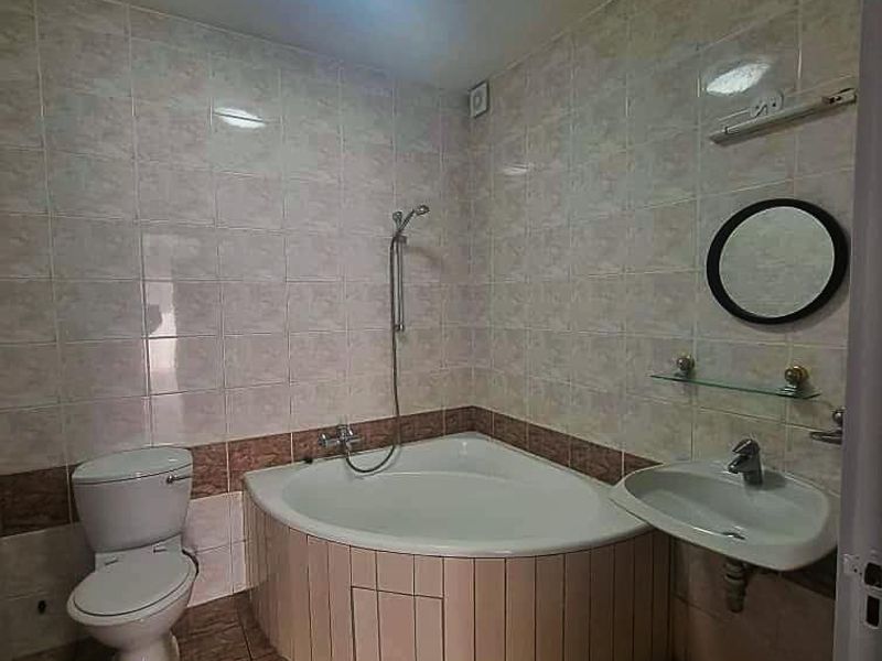 A functional bathroom featuring a corner bathtub, wall-mounted basin, and toilet with neutral tiled finishes throughout.